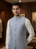 A man wearing a Sabhyashree light blue textured Nehru jacket over a white long-sleeve shirt, standing in a warm, dark wood-paneled indoor setting.
