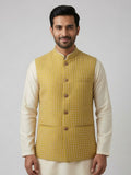 A man wearing Sabhyashree mustard yellow patterned Nehru jacket over cream-colored long-sleeve kurta pants, standing against a neutral gray studio background.